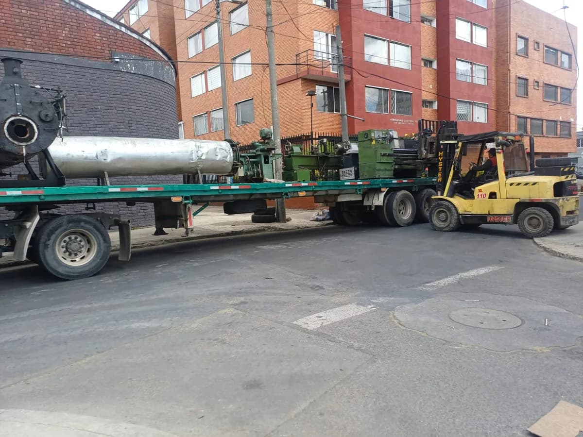 Camión de plataforma con carga voluminosa y montacargas apoyando el cargue